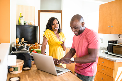 Image: Man and woman in a kitchen looking at a laptop smiling