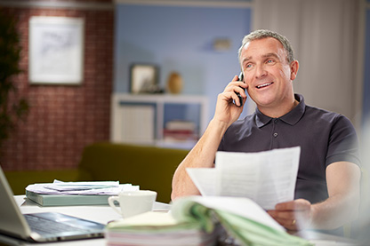 Image: Man on phone at table with papers in his hand