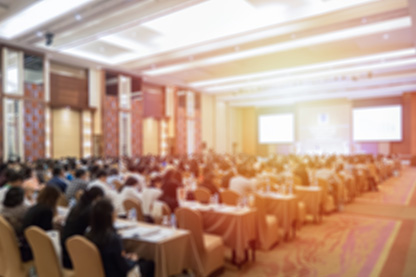 Image: Room full of people at tables facing a presentation at the front